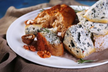 Mavi peynir dal biberiye, ekmek ve çuval bezi kumaş ve renk ahşap masa arka plan ile plaka üzerinde fındık ile