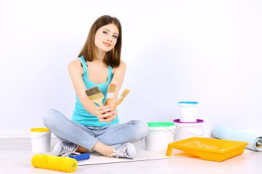 Güzel kız boyama duvar için ekipman ile katta oturan