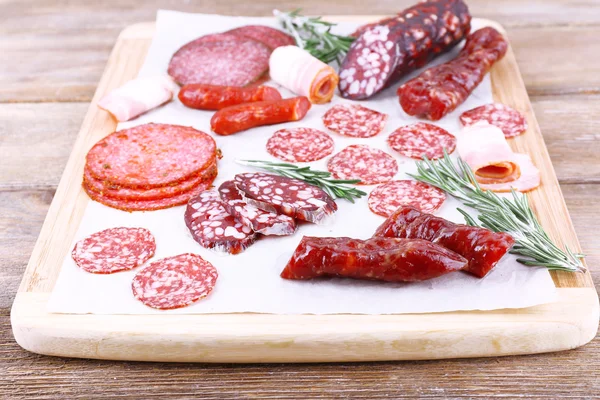 Assortment of sausages on cutting board and wooden table background — Stock Photo, Image