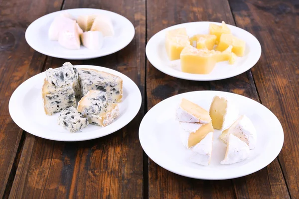 Various types of cheese on plates on wooden table background — Stock Photo, Image