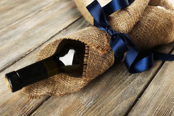 Wine bottle wrapped in burlap cloth on wooden planks background — Stock Photo, Image