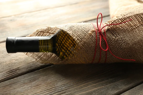 Wine bottle wrapped in burlap cloth on wooden planks background — Stock Photo, Image