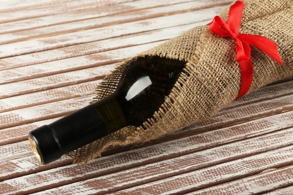 Botella de vino envuelta en tela de arpillera sobre tablones de madera fondo — Foto de Stock