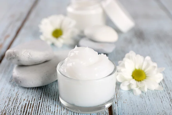 Creme cosmético com flores e pedras de spa em fundo de madeira — Fotografia de Stock