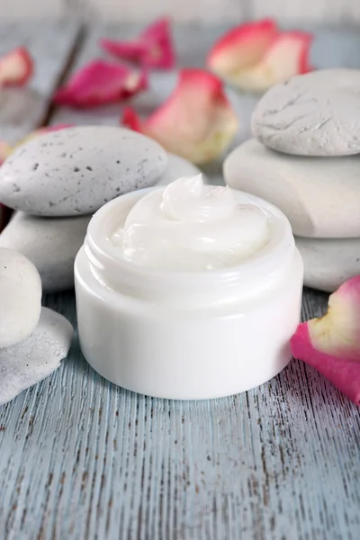 Crème cosmétique aux pétales de rose et pierres de spa sur fond de bois — Photo