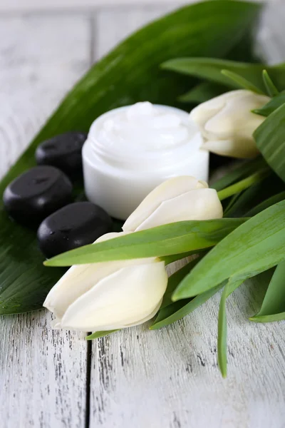 Crema cosmética con flores y piedras de spa sobre fondo de madera — Foto de Stock