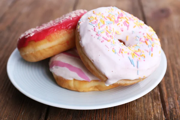 Delicious donuts with icing on plate on wooden background — Stock Photo, Image