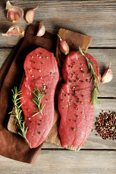 Rauwe biefstuk met rozemarijn en specerijen op snijplank op houten achtergrond — Stockfoto