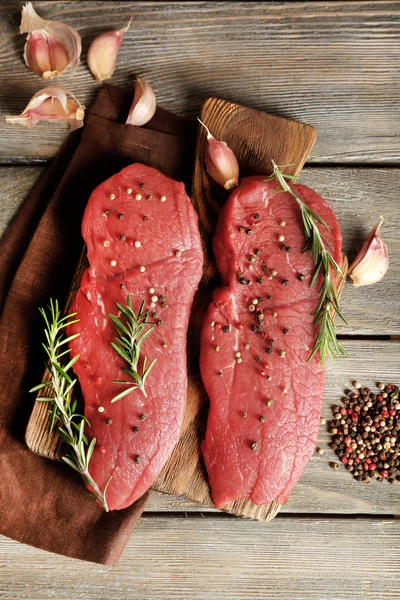 Steak de boeuf cru au romarin et épices sur planche à découper sur fond bois — Photo