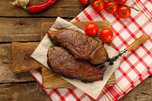 Composição com saborosa carne assada em tábua de corte, tomates e raminhos de alecrim em fundo de madeira — Fotografia de Stock