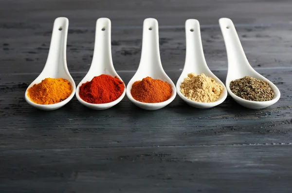 Different kinds of spices in spoons on wooden background — Stock Photo, Image