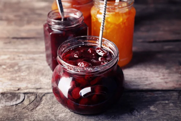 Gläser mit schmackhafter Marmelade auf hölzernem Hintergrund — Stockfoto