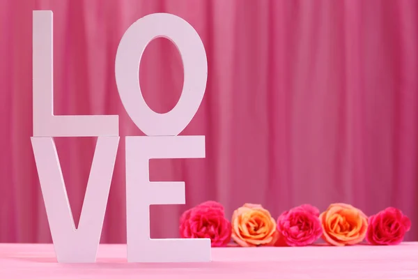 Letras decorativas formando palabra AMOR con flores sobre fondo rosa — Foto de Stock