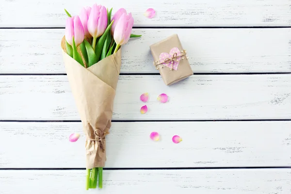 Schöne rosa Tulpen in Papier mit Geschenkschachtel auf Holzgrund — Stockfoto