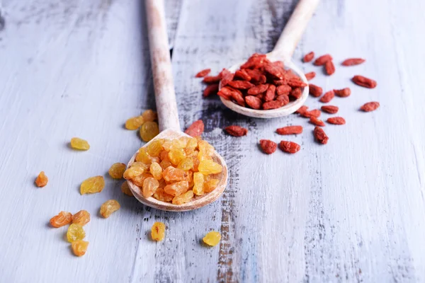 Pasas y Goji en cucharas sobre fondo de mesa de madera de color — Foto de Stock