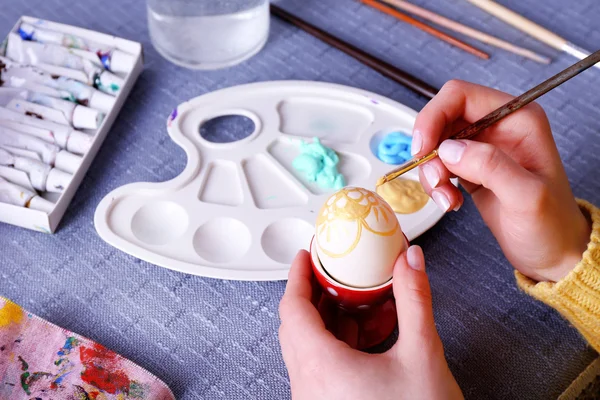 Pintura de ovos de Páscoa por mãos femininas em fundo de toalha de mesa colorido — Fotografia de Stock
