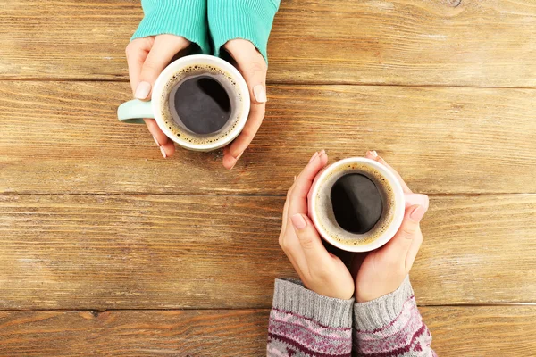 Mains féminines tenant des tasses de café sur fond de table en bois rustique — Photo