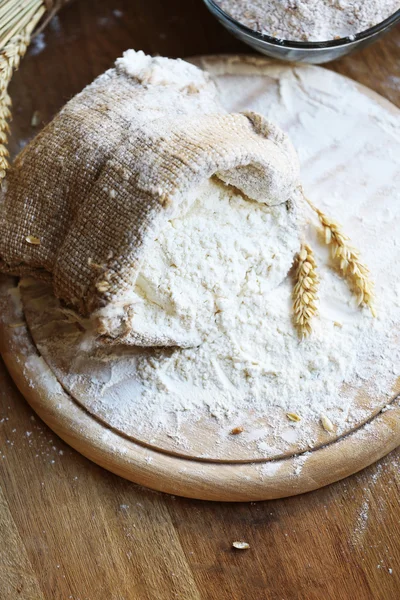 Flour in burlap bag on cutting board and wooden table background