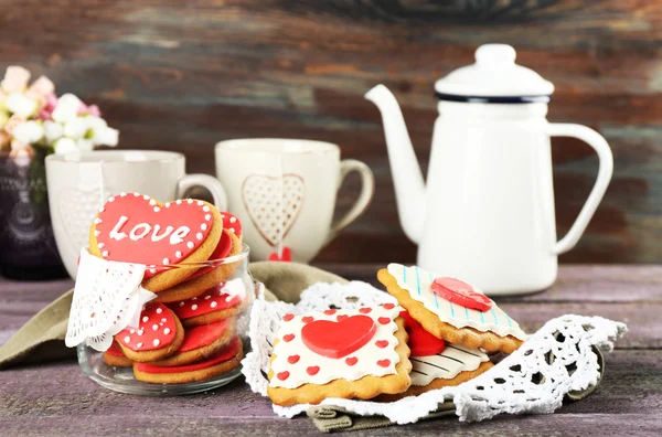 Herzförmige Plätzchen zum Valentinstag, Teekanne und Tassen auf farbigem Holzhintergrund — Stockfoto