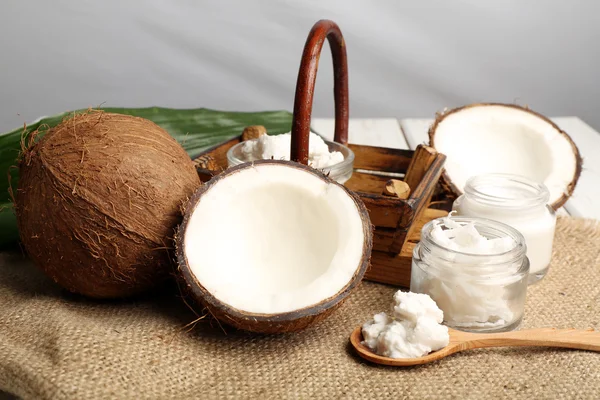 Coconut with jars of coconut oil and  cosmetic cream on sackcloth on light background — Stock Photo, Image