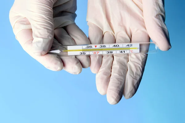 Hände mit Handschuhen halten Thermometer auf blauem Hintergrund — Stockfoto