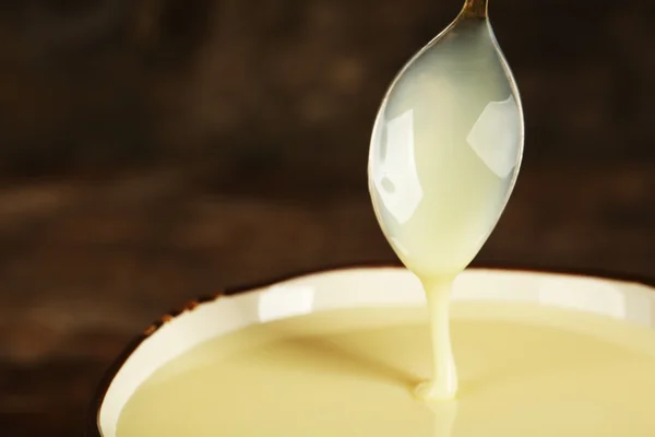 Miska z zagęszczonego mleka i łyżką na stole bliska — Zdjęcie stockowe