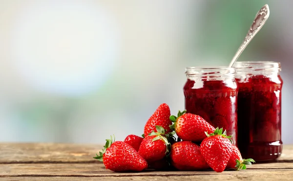 Frascos de mermelada de fresa con bayas en la mesa sobre fondo brillante — Foto de Stock