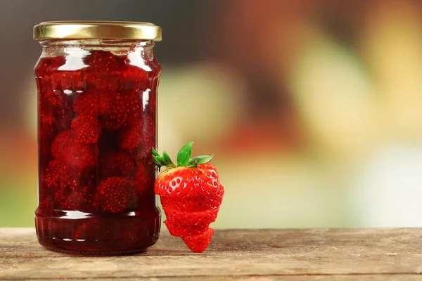 Jar of strawberry jam with sliced berry on table on bright background — Stock Photo, Image