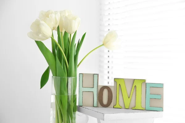 Casa em letras coloridas e flores de primavera em interior branco claro — Fotografia de Stock