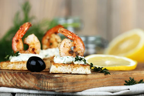Appetizer canape with shrimp and lemon on cutting board on table close up — Stock Photo, Image