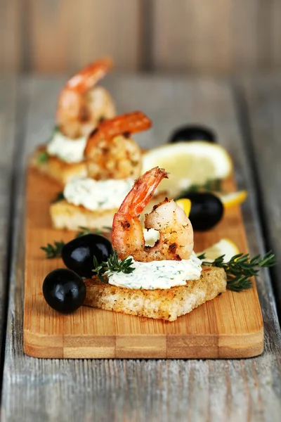 Canapé de aperitivo com camarão e azeitonas em fundo de madeira — Fotografia de Stock