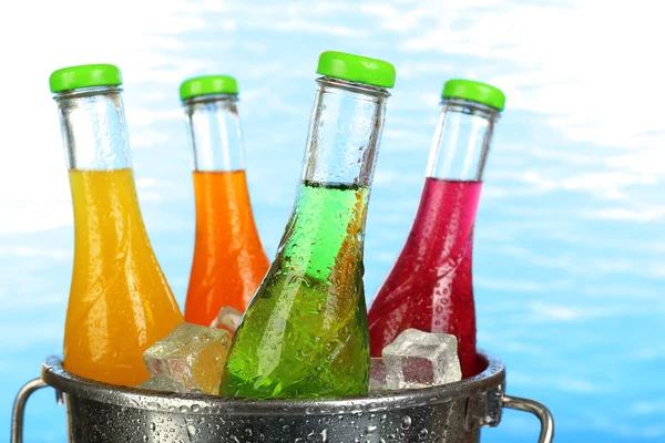 Bottles of tasty drink in metal bucket with ice on bright background — Stock Photo, Image