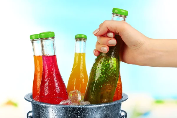 Female hand taking glass bottle of drink from metal bucket on bright background — Stock Photo, Image