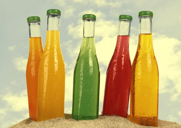 Бутылки вкусного напитка на песке изолированы на белом — стоковое фото