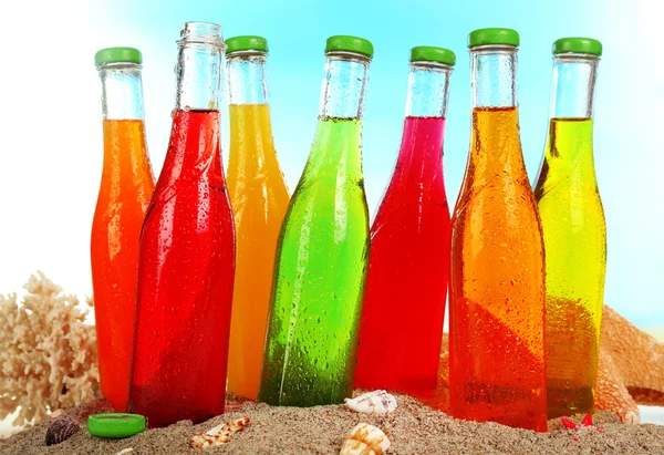 Bottles of tasty drink on sand on bright background — Stock Photo, Image