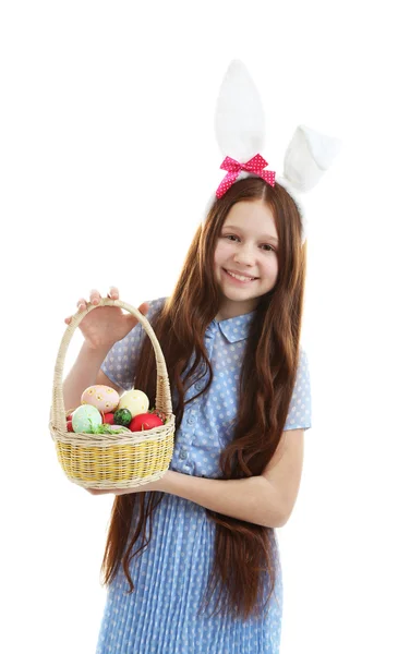 Beautiful little girl wearing Easter bunny ears and holding wicker basket with Easter eggs, isolated on white — Stock Photo, Image