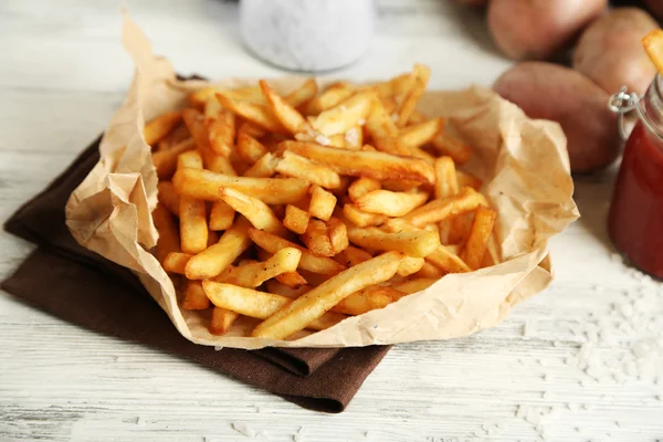 Tasty french fries on paper napkin, on wooden table background