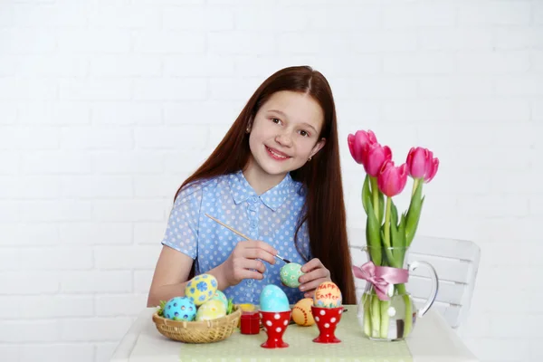 Cute girl decorates Easter eggs, on light background — Stock Photo, Image