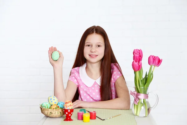 Милая девушка украшает пасхальные яйца, на светлом фоне — стоковое фото