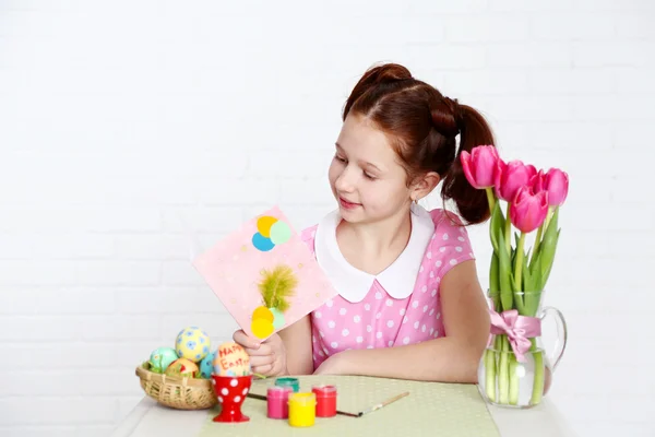 Cute girl  with greeting card and decorated Easter eggs, on light background — Stock Photo, Image
