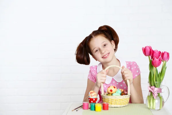 Leuk meisje siert paaseieren, op lichte achtergrond — Stockfoto