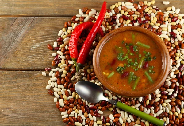 Soupe de haricots dans un bol et haricots crus sur fond de table en bois — Photo