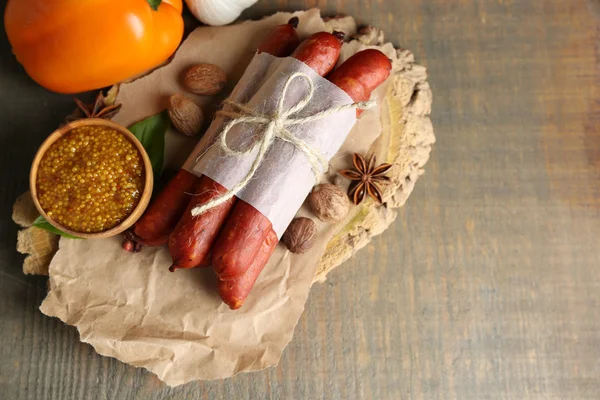 Composition of smoked thin sausages, mustard in bowl and spices on cutting board, on wooden background — Stock Photo, Image