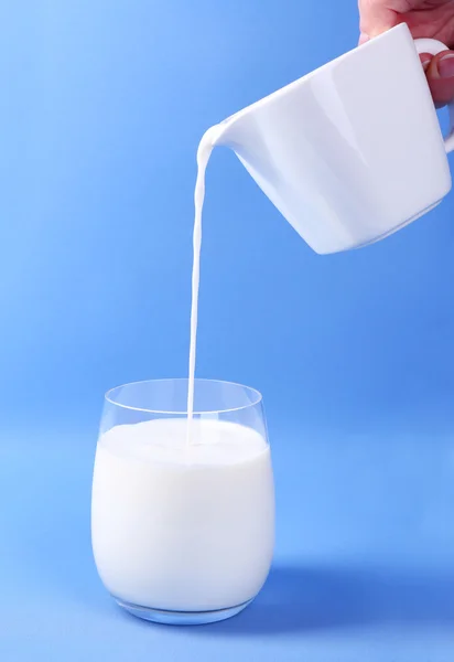 Verter la leche en un vaso sobre fondo azul — Foto de Stock