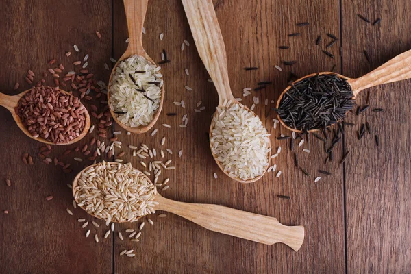 Diferentes tipos de arroz en cucharas sobre fondo de madera — Foto de Stock