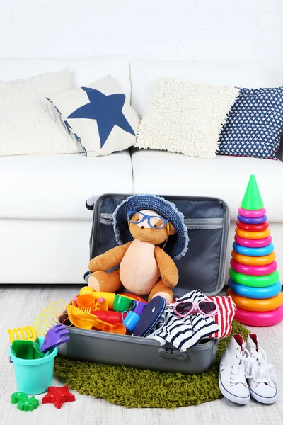 Valise remplie de vêtements et de jouets pour enfants sur tapis en fourrure et fond de canapé blanc — Photo