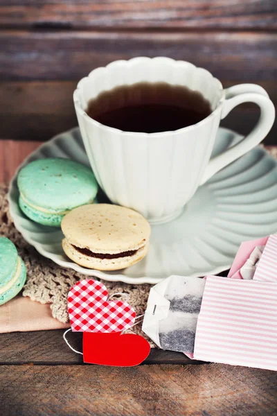 Heart shaped teabag tags, macaroons and cup of tea on wooden background — Stock Photo, Image