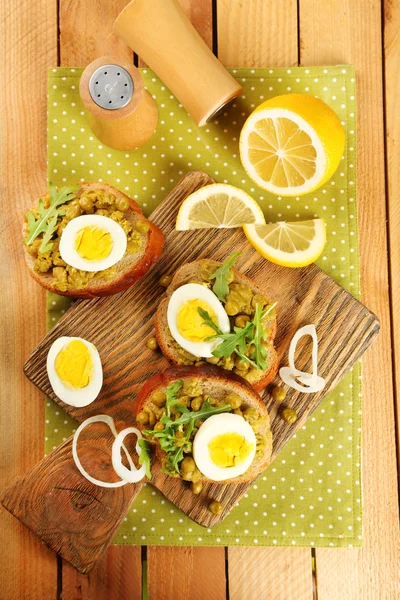 Sandwiches with green peas paste and boiled egg on cutting board with napkin on wooden planks background — Stock Photo, Image