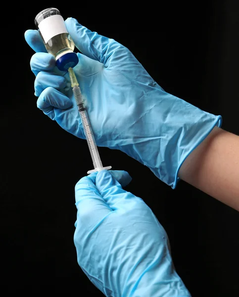 Mani nei guanti che riempiono il medicinale dalla fiala alla siringa su fondo nero — Foto Stock