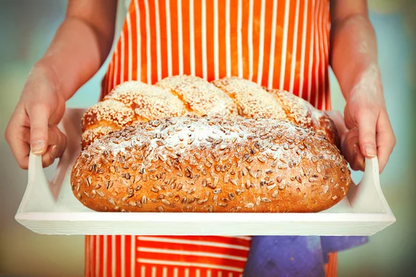 Traditional bread in female hands on wooden tray on light blurred background — Stock Photo, Image